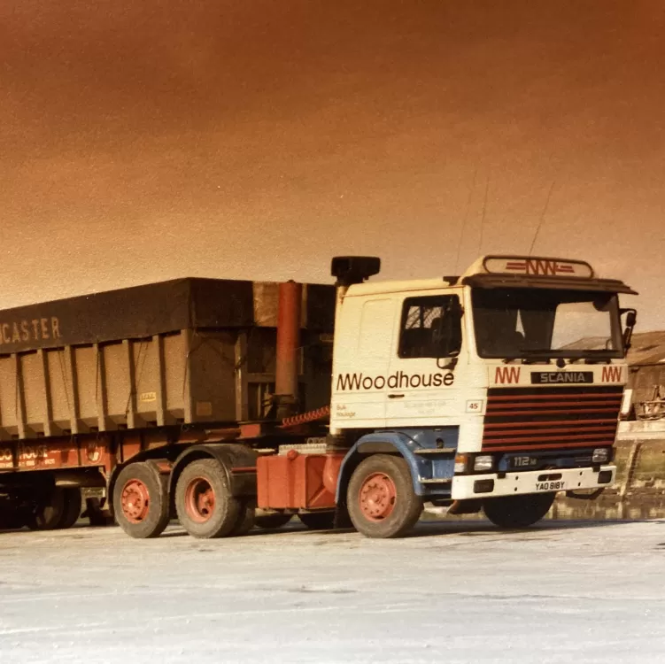 A classic M.Woodhouse Transport Ltd Scania truck carrying a loaded tipper trailer, symbolising the company's long-standing service in the haulage industry.